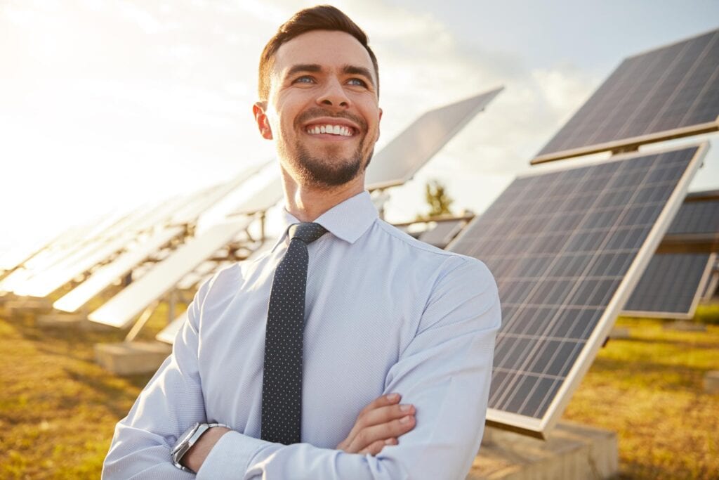 Hombre trajeado sonriendo en frente de placas solares. 