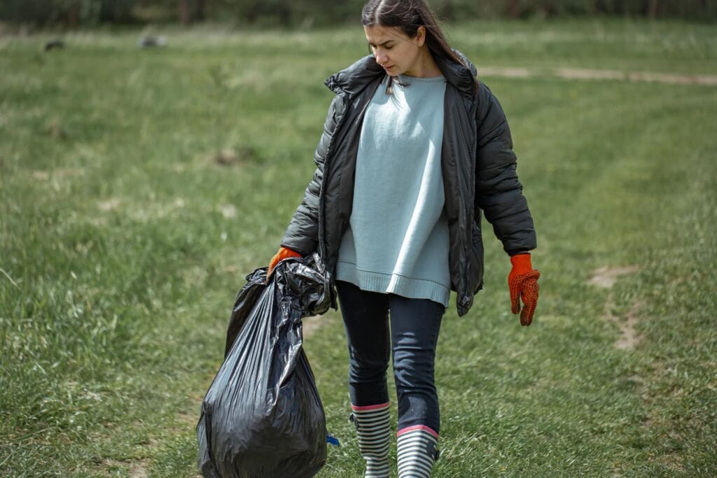 Chica con una bolsa de basura recogiendo en un campo.