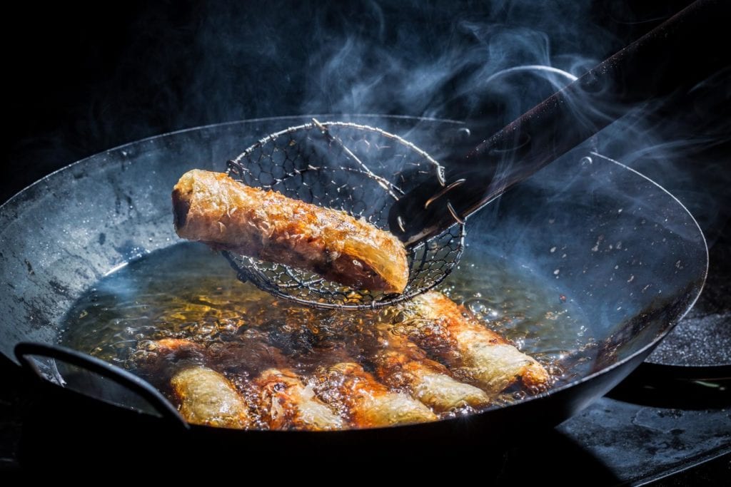 Rollitos de primavera friéndose en aceite caliente en una sartén, ilustrando el manejo de aceites en cocinas de hostelería.