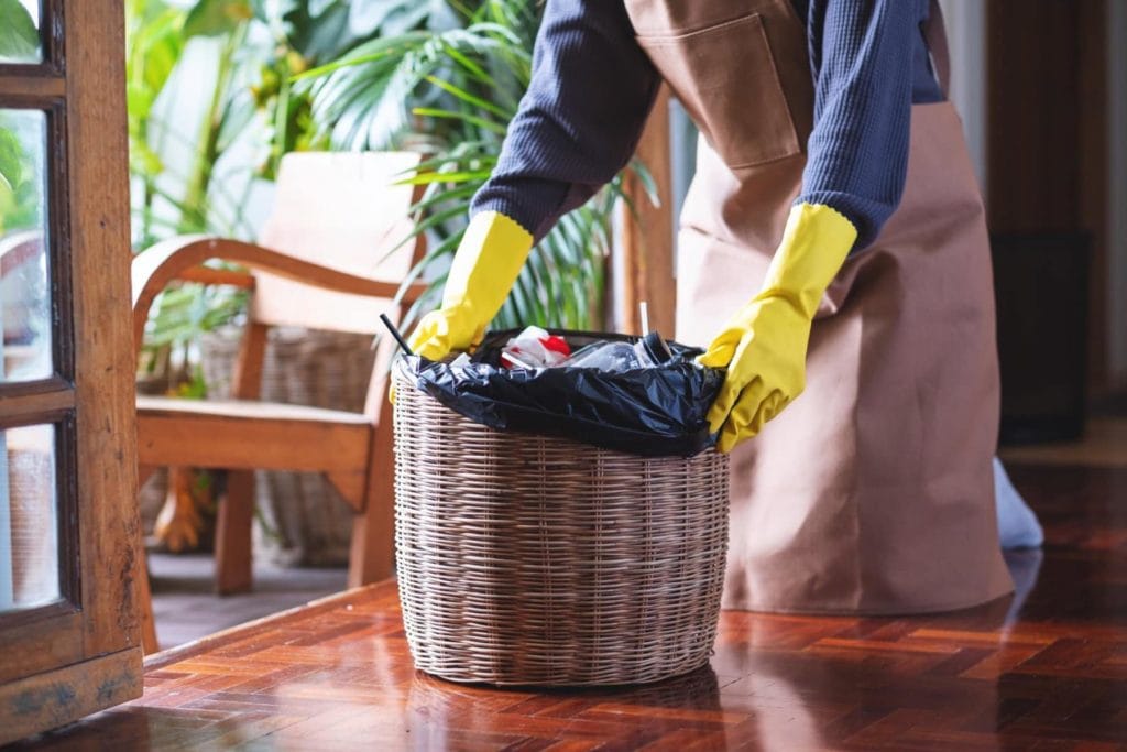 Persona colocando una bolsa de basura reciclada en un cesto de mimbre, destacando su uso en espacios interiores y su compromiso con el medio ambiente.