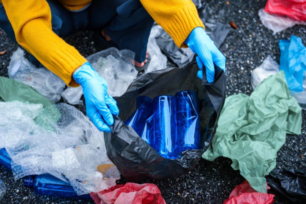 Persona clasificando residuos y botellas de plástico con guantes protectores, representando una gestión eficiente de residuos en invierno.