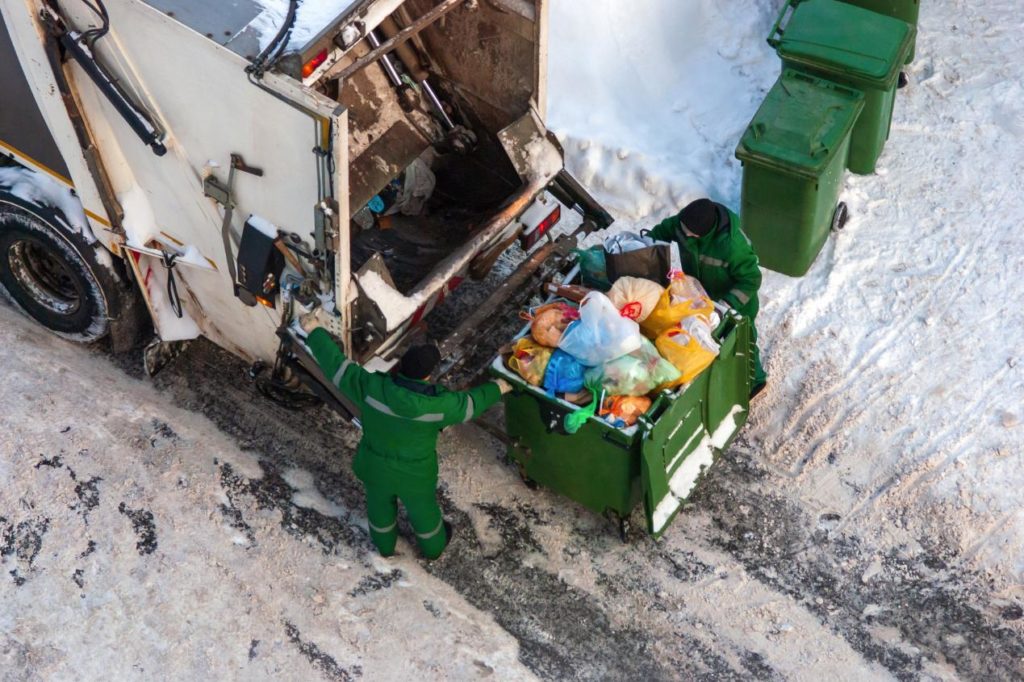 Trabajadores de recolección de residuos en invierno vaciando contenedores en un camión de basura, ilustrando la gestión de residuos en condiciones climáticas frías.