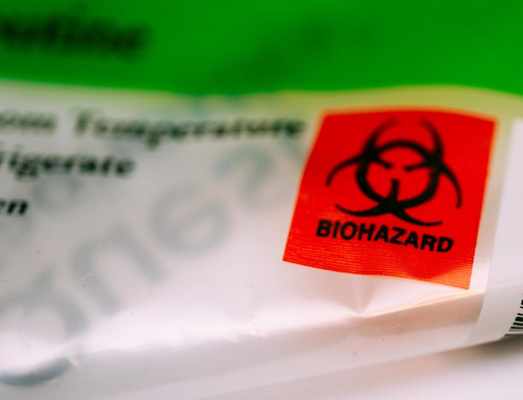 Primer plano de un sello rojo con el símbolo de biohazard en una bolsa de residuos médicos, indicando peligro biológico.