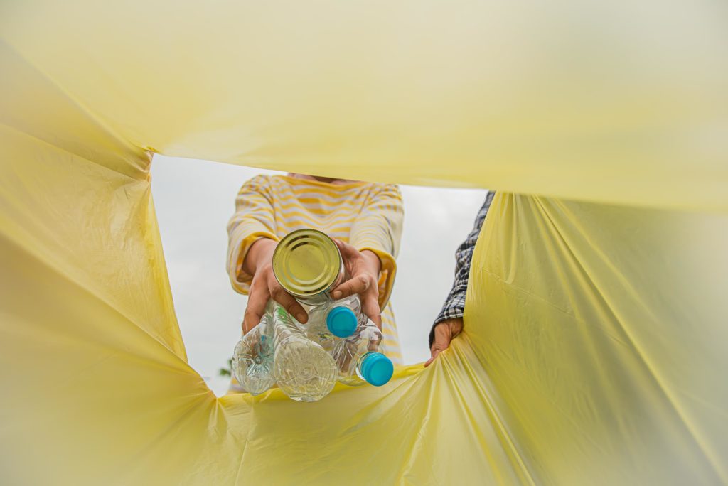 Persona depositando botellas de plástico y una lata en una bolsa amarilla de reciclaje, destinada a envases ligeros y metálicos