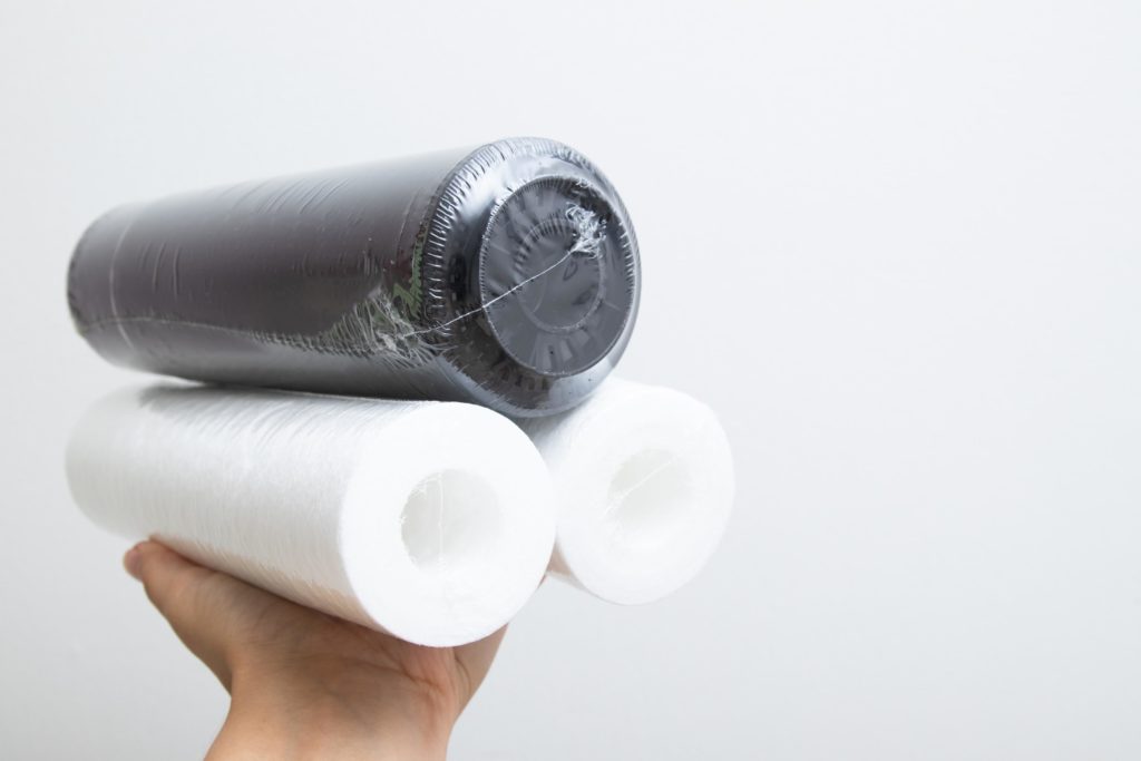Mano sosteniendo rollos de bolsas recicladas y compostables, en su embalaje original para conservarlas protegidas de la humedad y el polvo