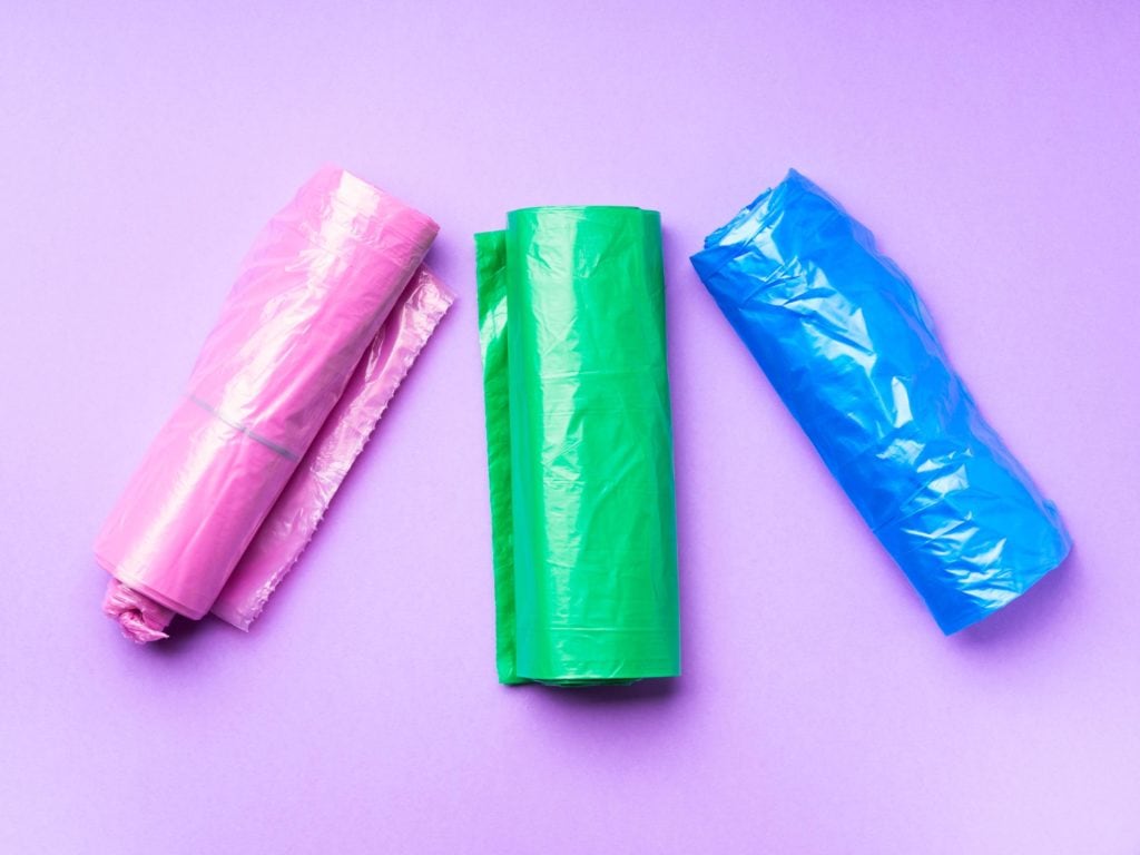 Rollos de bolsas de plástico en colores fucsia, verde y azul sobre fondo lila.