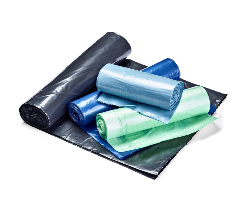 Surtido de rollos de bolsas de basura recicladas en colores negro, azul y verde para la clasificación selectiva de residuos en almacenes y logística.
