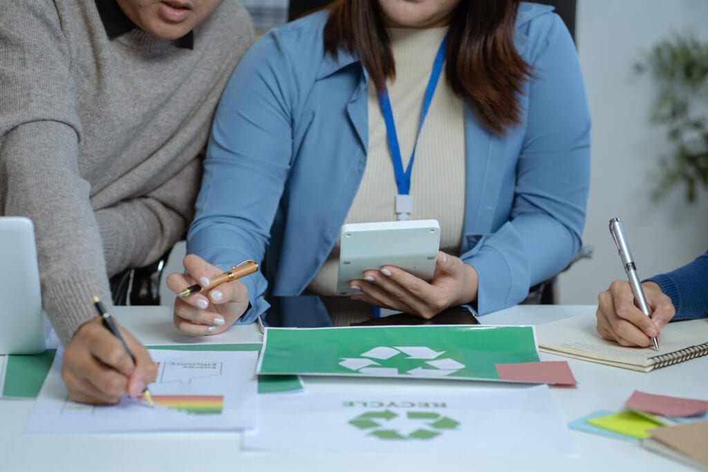 quipo de trabajo en una reunión corporativa analizando costes y estrategias de sostenibilidad, con gráficos de gestión de residuos y símbolos de reciclaje sobre la mesa.